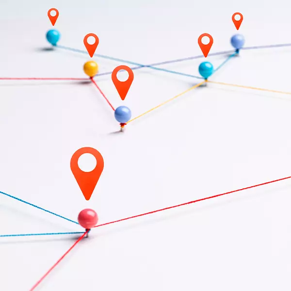 Representação de um mapa feito com alfinetes coloridos interligados por linhas em um fundo branco, simulando conexões, com ícones de localização vermelhos destacando certos pontos.